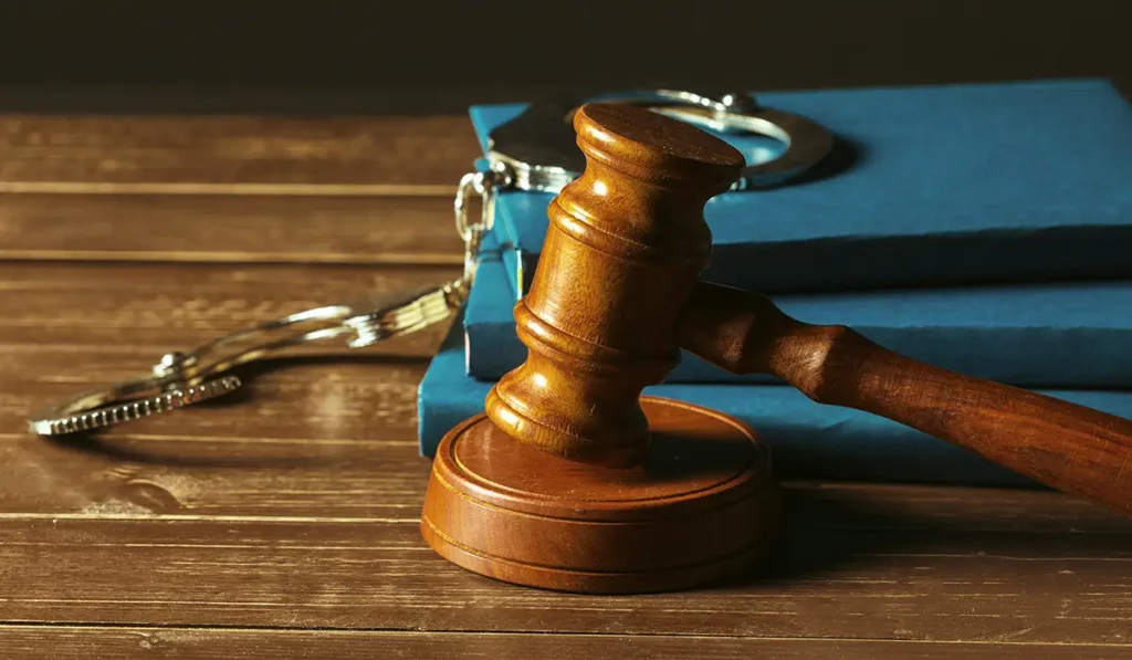 Wooden gavel on a desk with legal books and handcuffs representing a criminal defense lawyer.