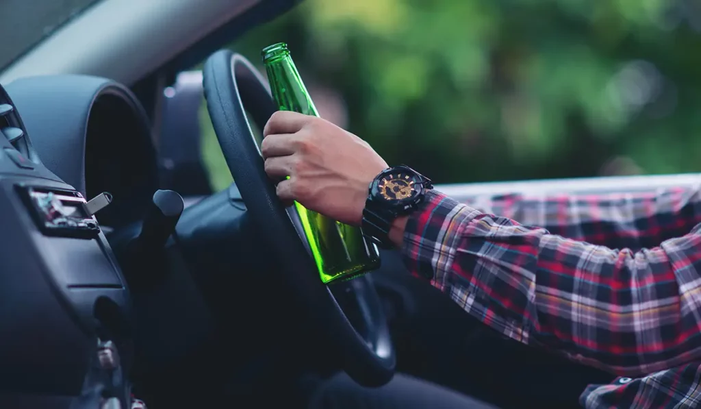 Driver holding a beer bottle in a car, highlighting the importance of Chicago DUI Attorneys services.