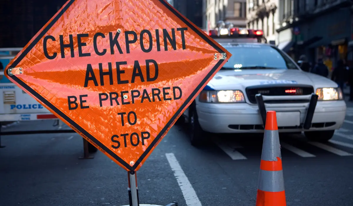 Bright orange warning sign reading “Checkpoint Ahead Be Prepared to Stop” placed before police car during Illinois DUI checkpoints.